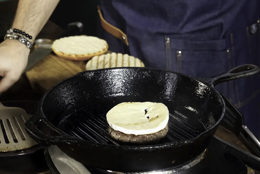 Burger patty with cheese cooking in a cast iron grill pan