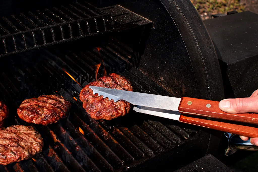 Burgers sizzling on the grill, flipped with tongs
