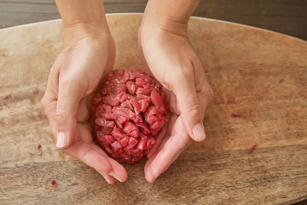 Ground beef being shaped into patties on a wooden cutting board